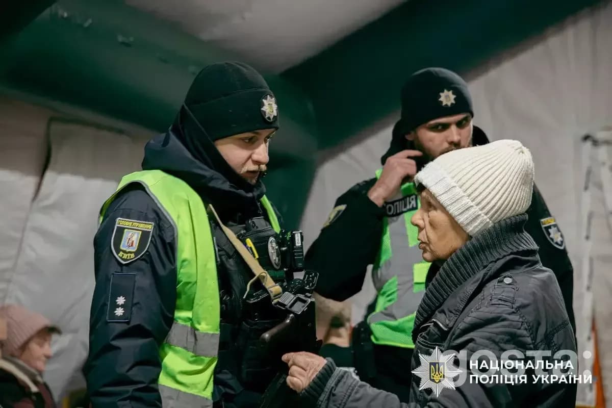 Троє поліцейських Нацполіції України допомагають людям у зимовому одязі в наметі, Київ, 2026 рік.