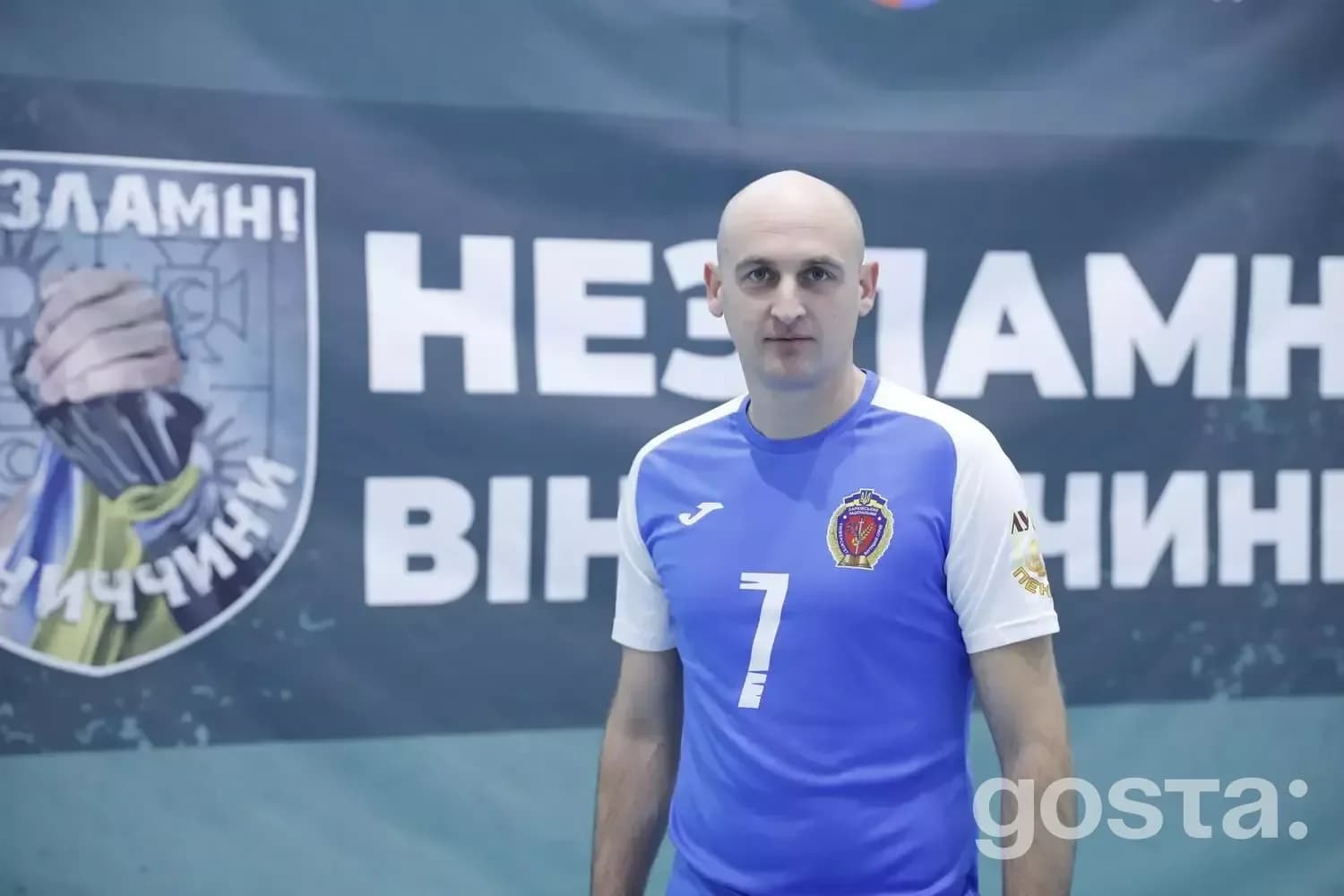 До зображення входить портрет чоловіка у синьо-білій футболці з номером 7 на тлі банера.