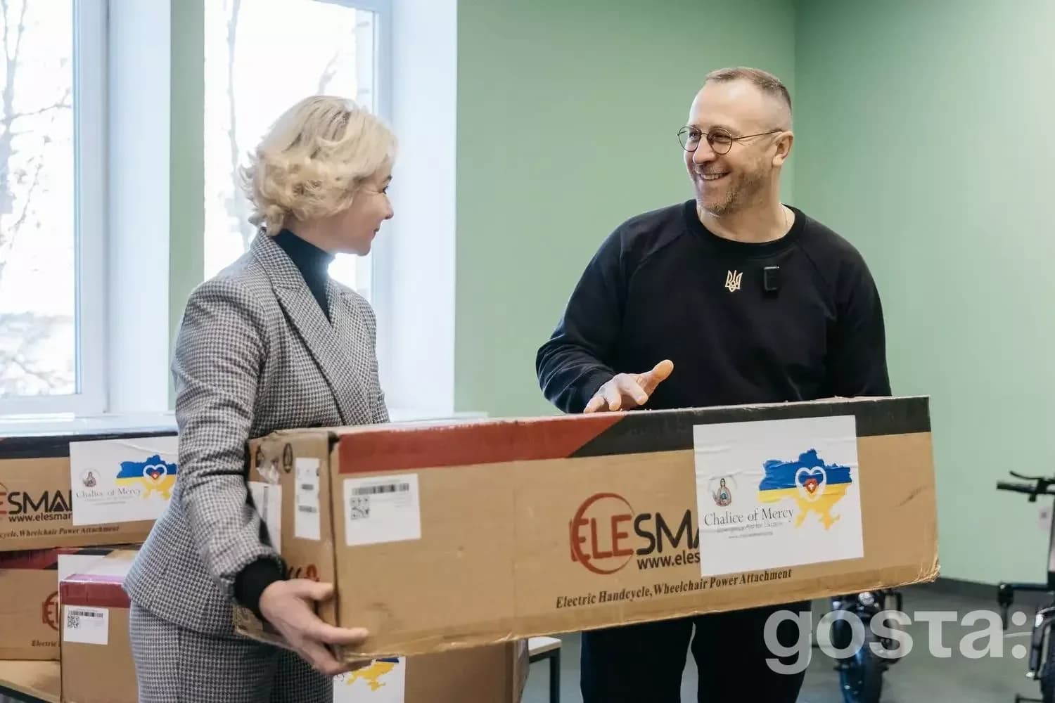 Дві особи обговорюють коробку з логотипом Elesma у приміщенні госпіталю, присвяченому реабілітації ветеранів МВС.