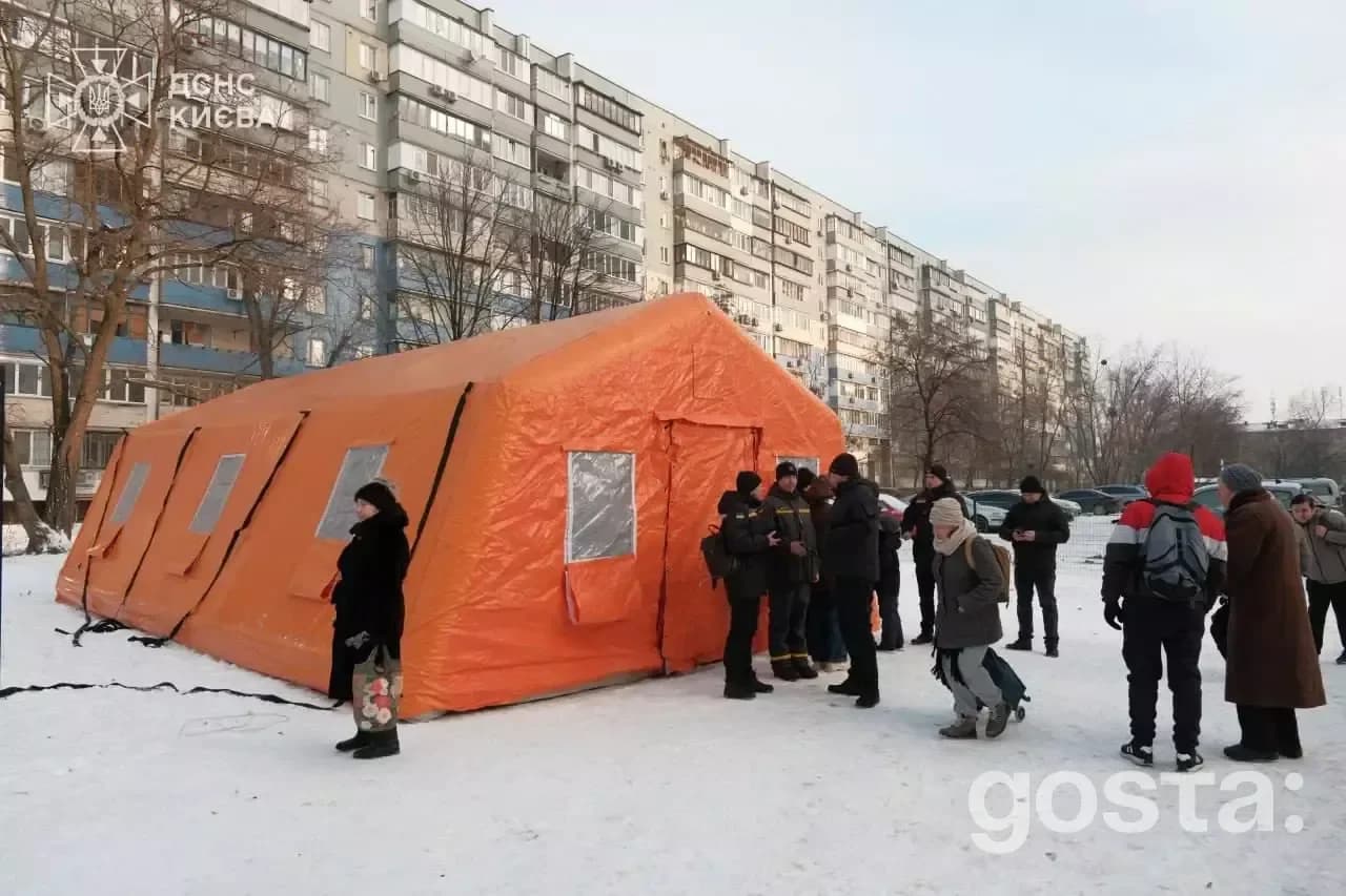 Люди збираються біля помаранчевого намету ДСНС Києва на снігу серед багатоповерхівок у зимовий день.