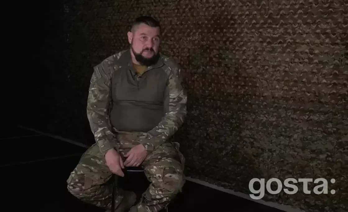 Боєць Нацполіції України у камуфляжі сидить перед камуфляжним фоном, розповідаючи свою історію війни.