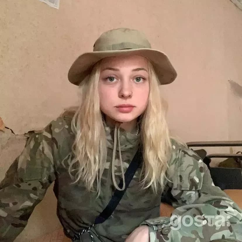 На фото зображено молода жінка у камуфляжі, зосереджена та готова до служби.