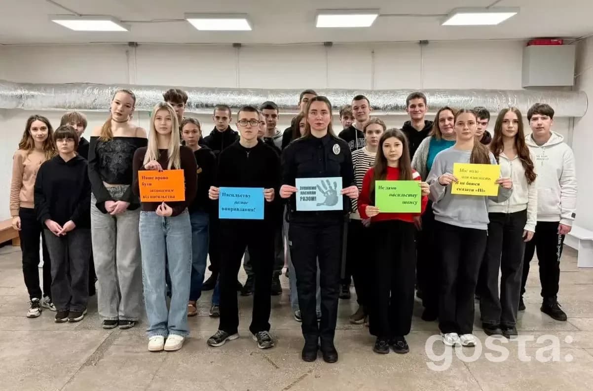 Група молоді та офіцерка поліції з плакатами в освітньому закладі сприяють безпеці та довірі.