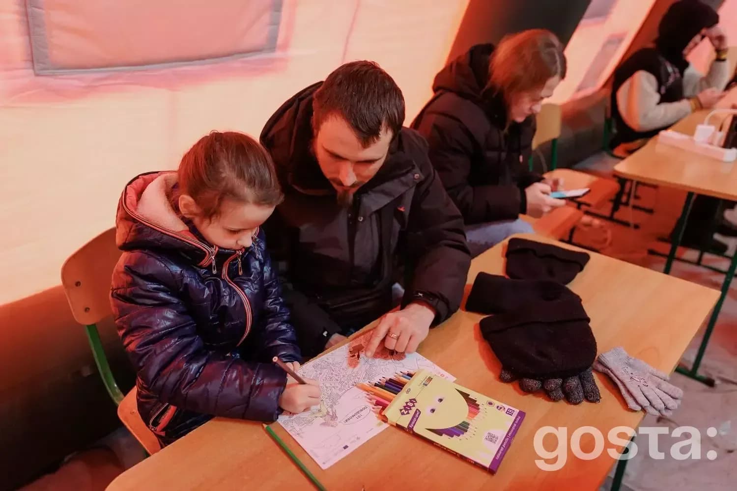 Люди в укритті під час обстрілу в Україні; дитина малює разом з дорослим, інші користуються телефонами.
