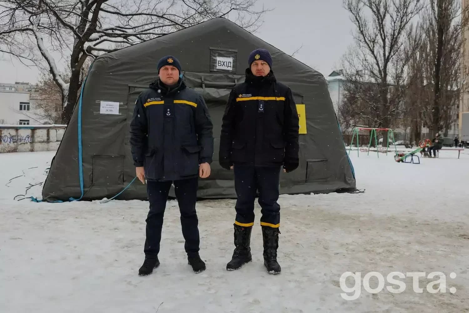 На фото два рятувальники стоять перед швидкомонтованим пунктом обігріву на засніженій території.