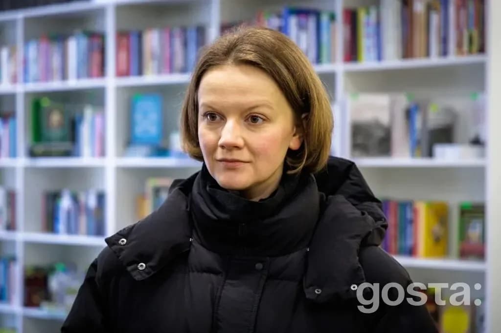На зображенні жінка на фоні книжкових полиць у бібліотеці. Візит задля підтримки культурних ініціатив.