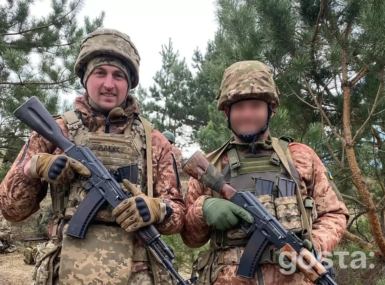 На фото двоє військовослужбовців у камуфляжній формі з автоматами стоять серед дерев.
