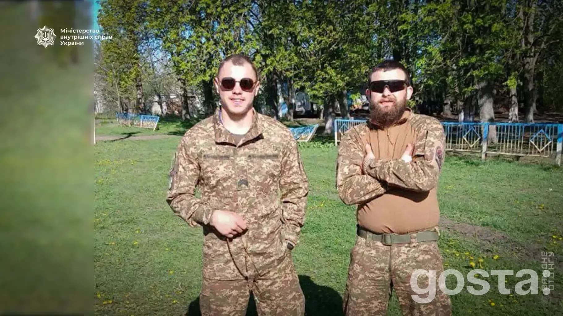 Двоє українських гвардійців у формі стоять на зеленому полі на тлі дерев.