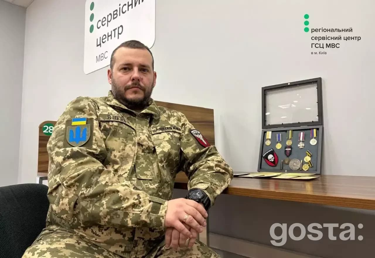 Ветеран у військовій формі сидить у сервісному центрі МВС, поруч з нагородами, демонструючи служіння державі.