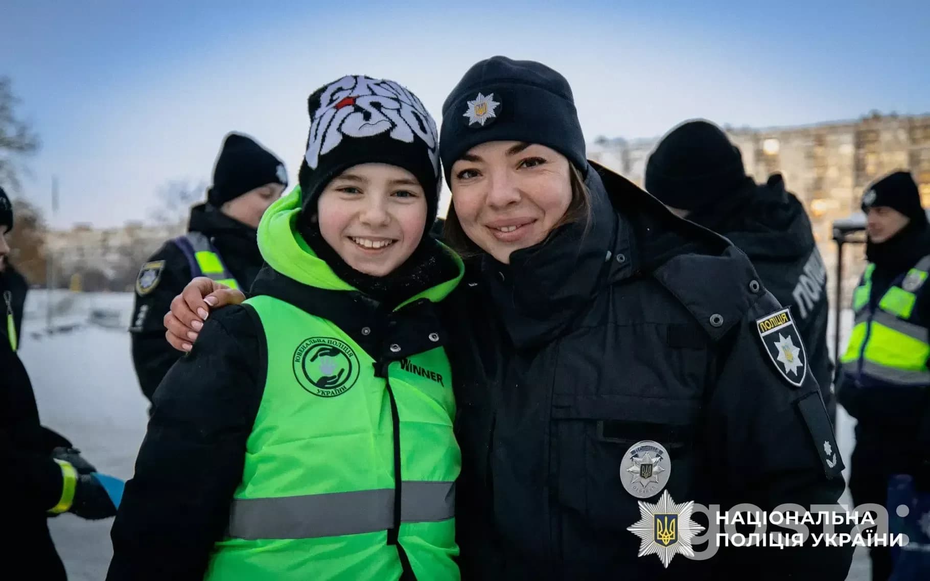На зображенні усміхнені ювенальні поліцейські з дитиною в зимовий час, Одягнені у форму зі світловідбивальними елементам