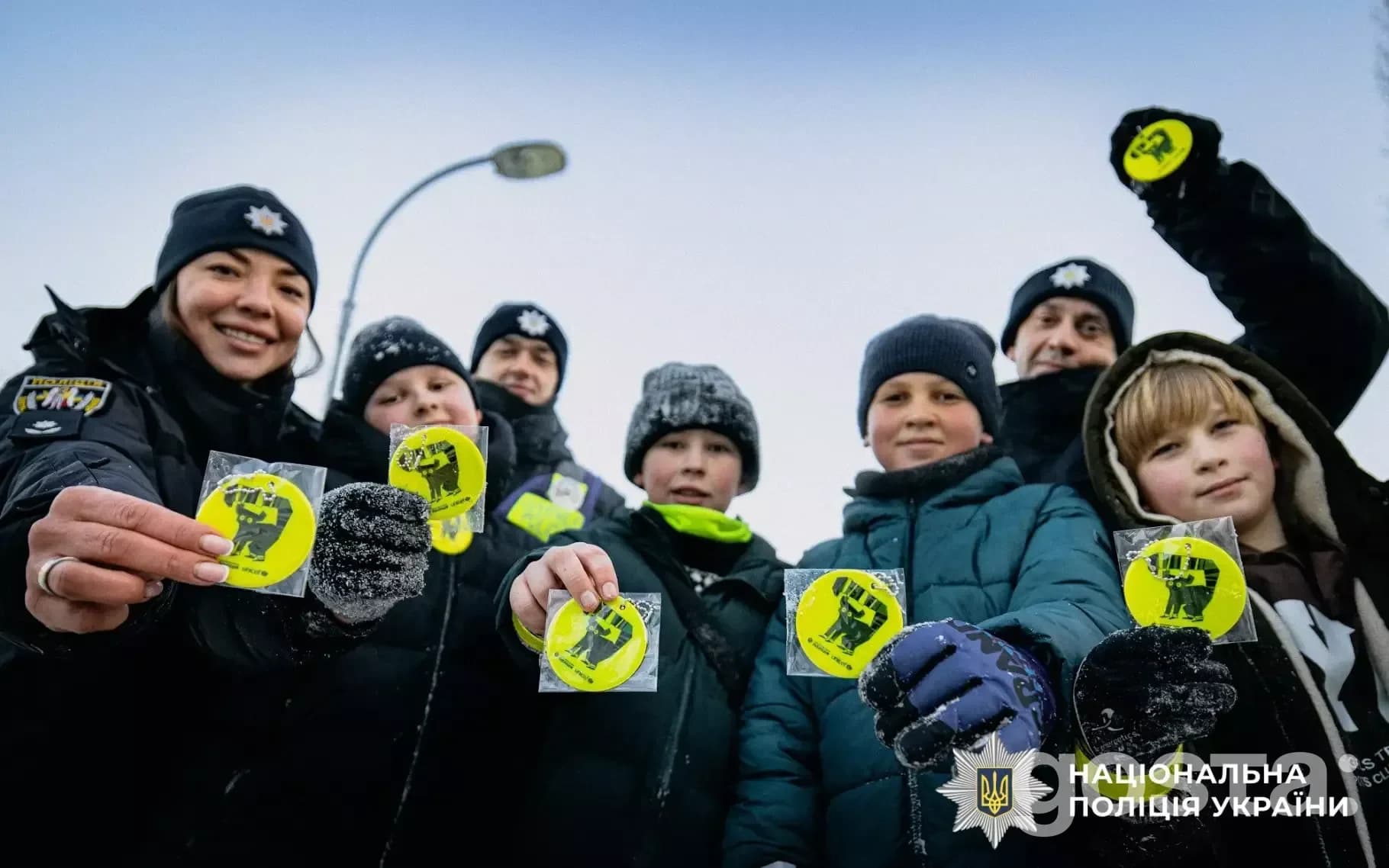 Ювенальні поліцейські роздають дітям світловідбивні елементи для безпеки на дорозі взимку.