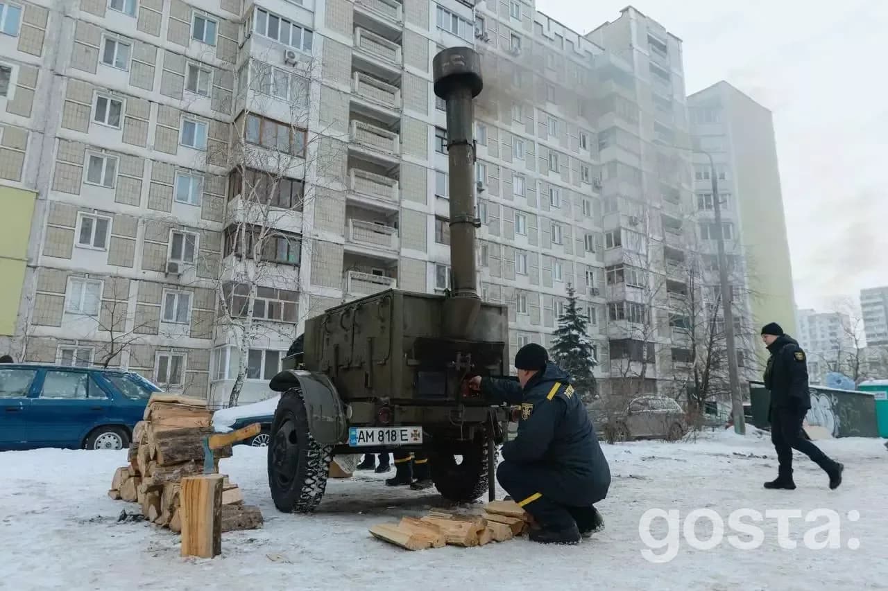 На фото зображено рятувальника біля мобільного пункту обігріву в зимовий час у дворі багатоповерхівки в Києві.