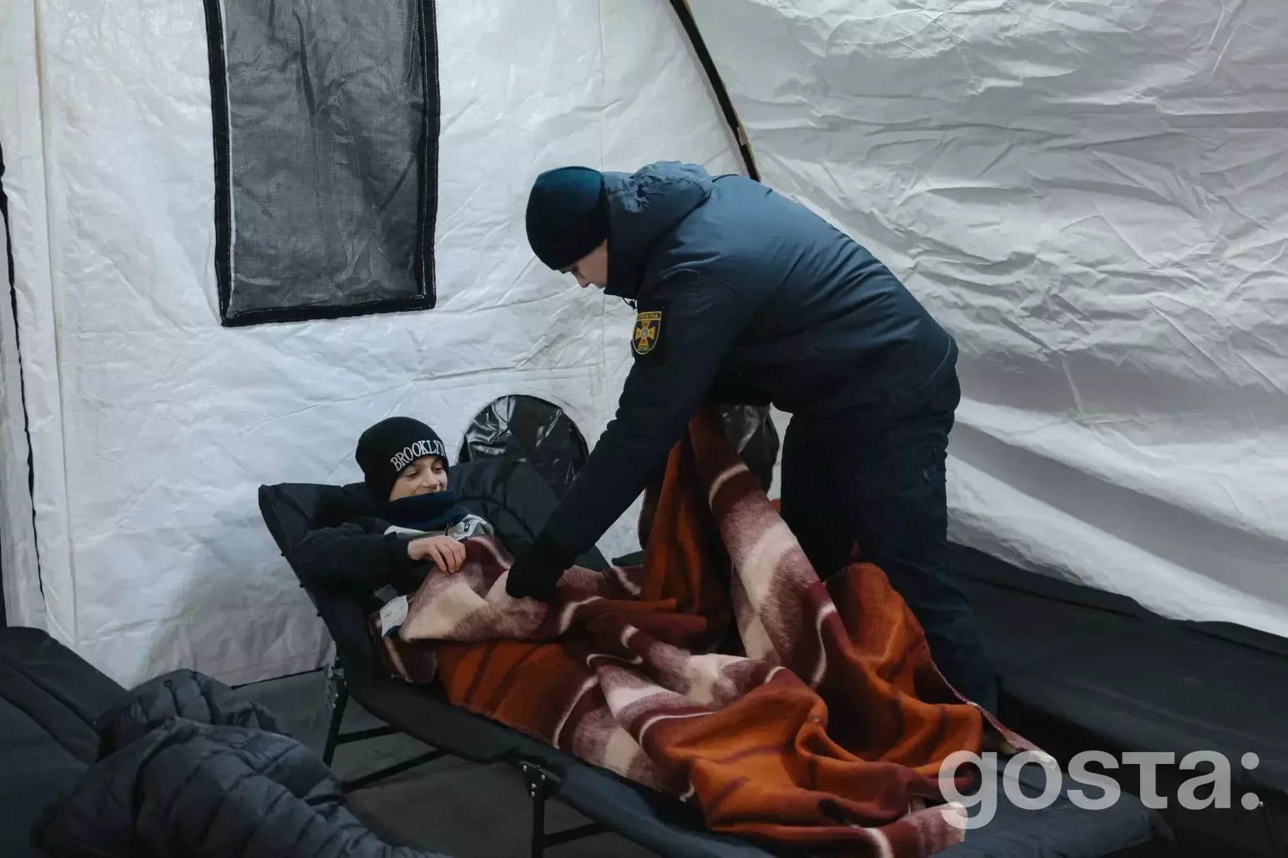 Рятувальник ДСНС допомагає дитині в наметовому містечку в Троєщині після обстрілів; облаштовано пункти обігріву.