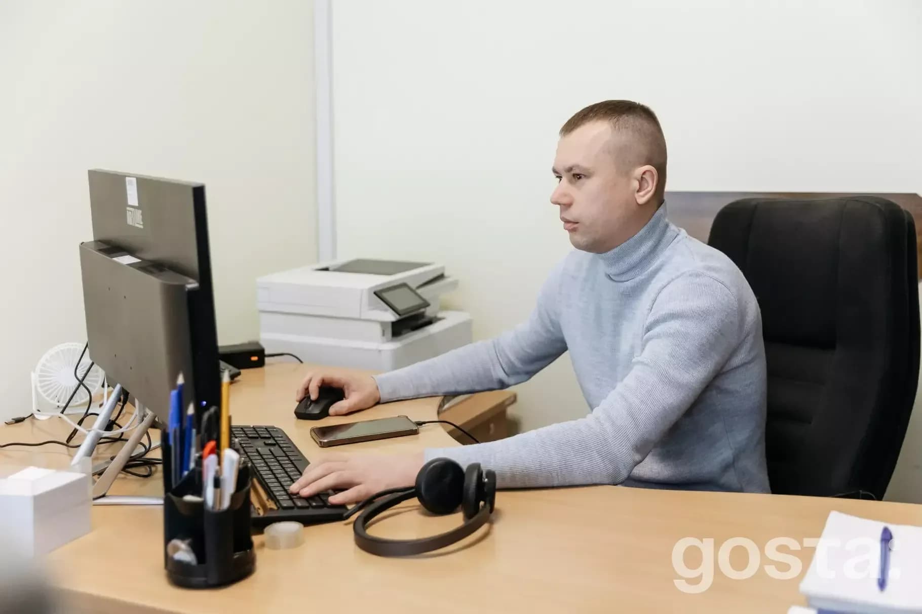 Чоловік працює за комп'ютером в офісі, бездротові навушники на столі, займається обробкою дзвінків для контактного центр