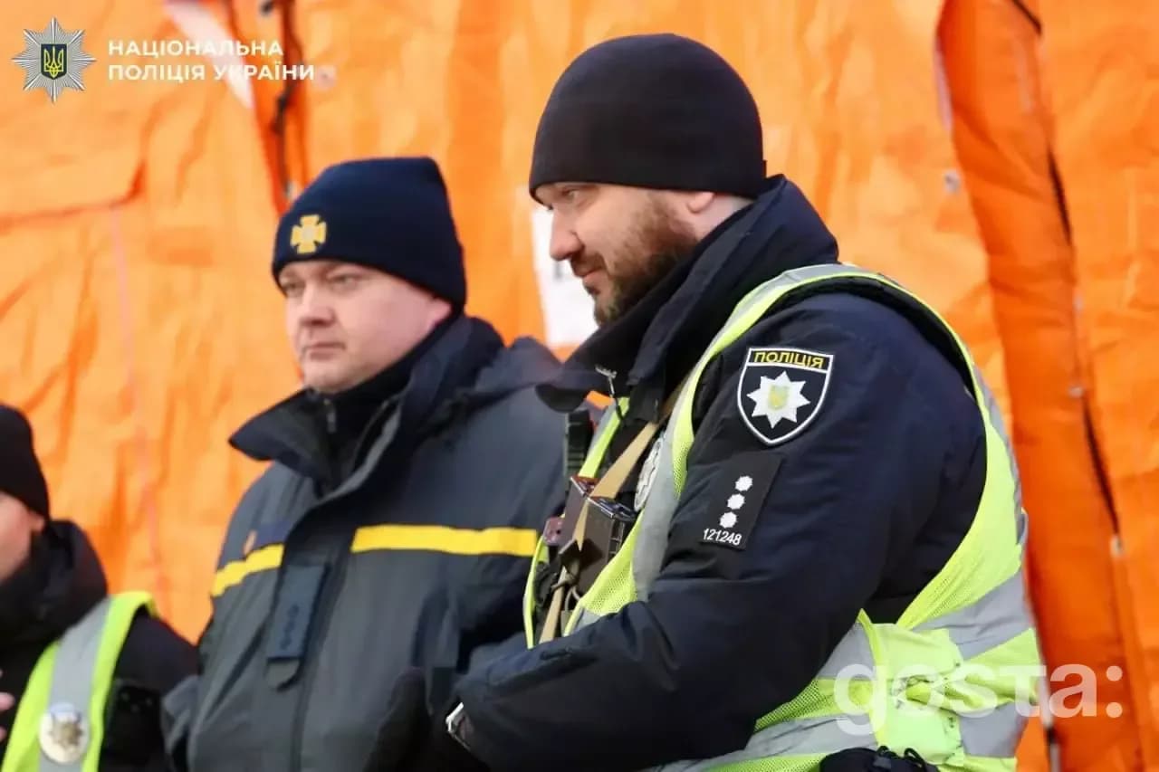 Двоє поліцейських Нацполіції України на службі в зимовому одязі на фоні помаранчевих наметів.