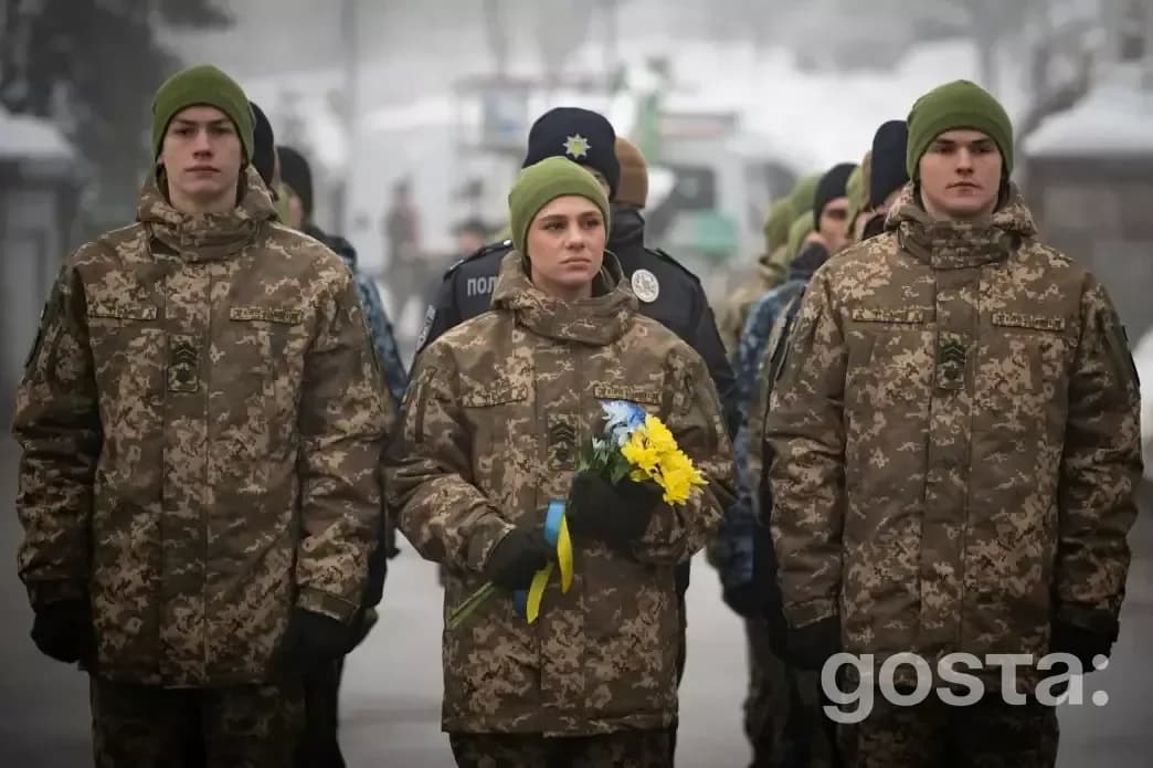 Військові в камуфляжі під час вшанування пам'яті Героїв Крут у Києві, жінка тримає букет з жовтими та синіми квітами.