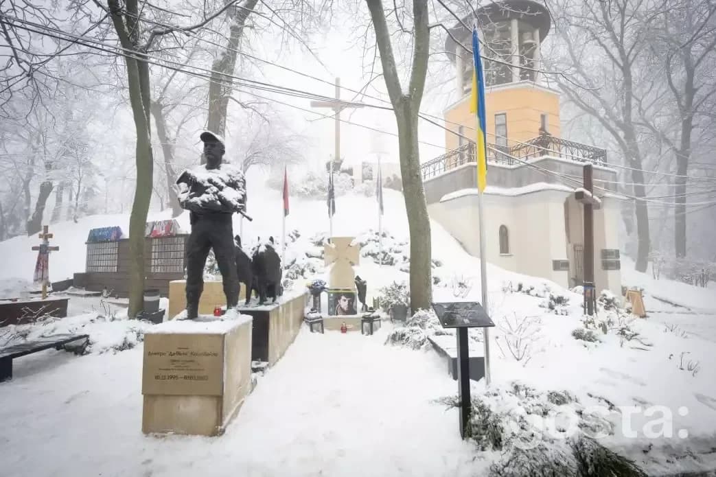 На фото засніжене кладовище з пам'ятником і хрестом. Пам'ять Героїв Крут вшановується в Києві.