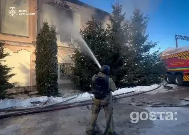 На зображенні рятувальник гасить полум'я біля будівлі в зимовий час.
