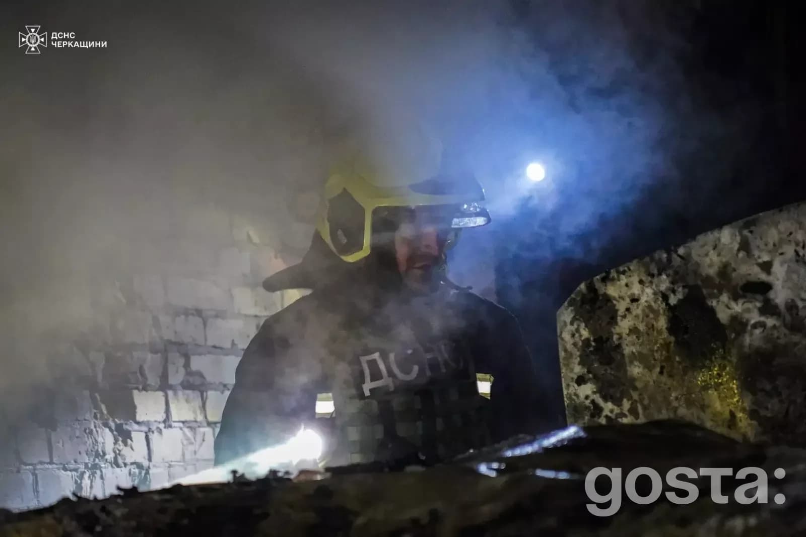 Рятувальник у захисному одязі проводить огляд пошкодженої будівлі після обстрілів у Донеччині та Черкащині, дим навколо.