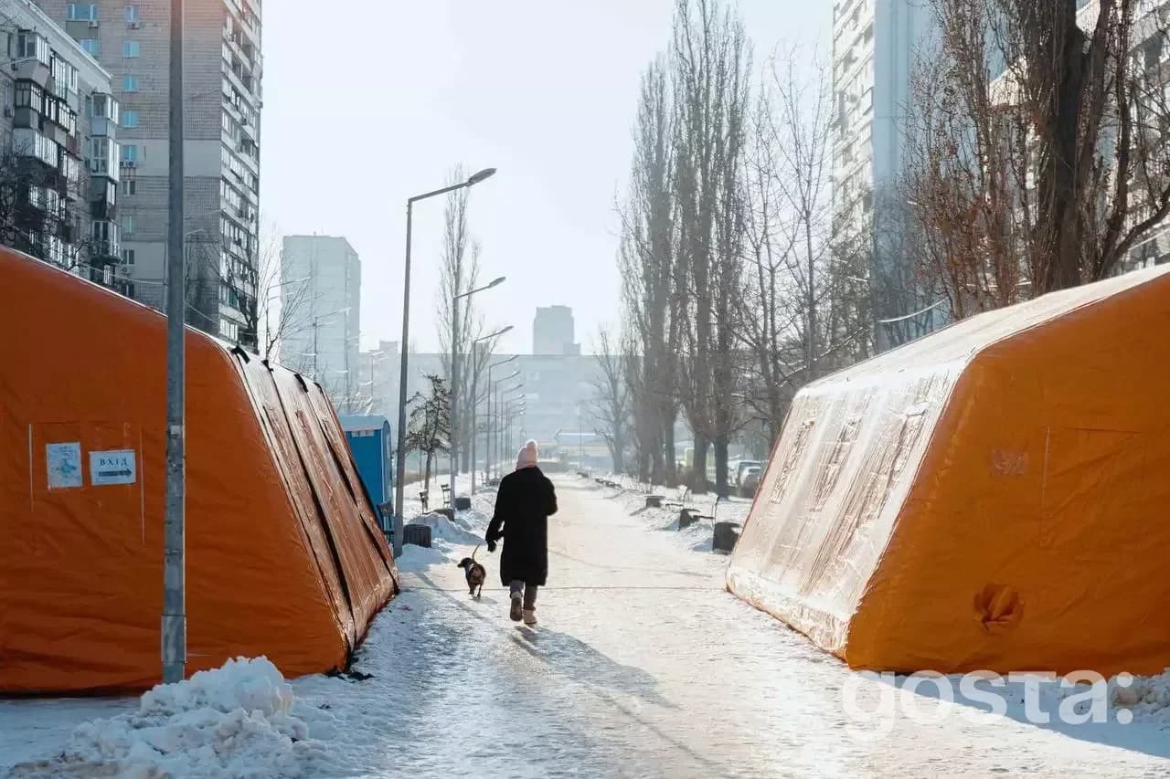 Не знаю, хто зображений. Помаранчеві намети обігріву на засніженій міській вулиці між висотками.