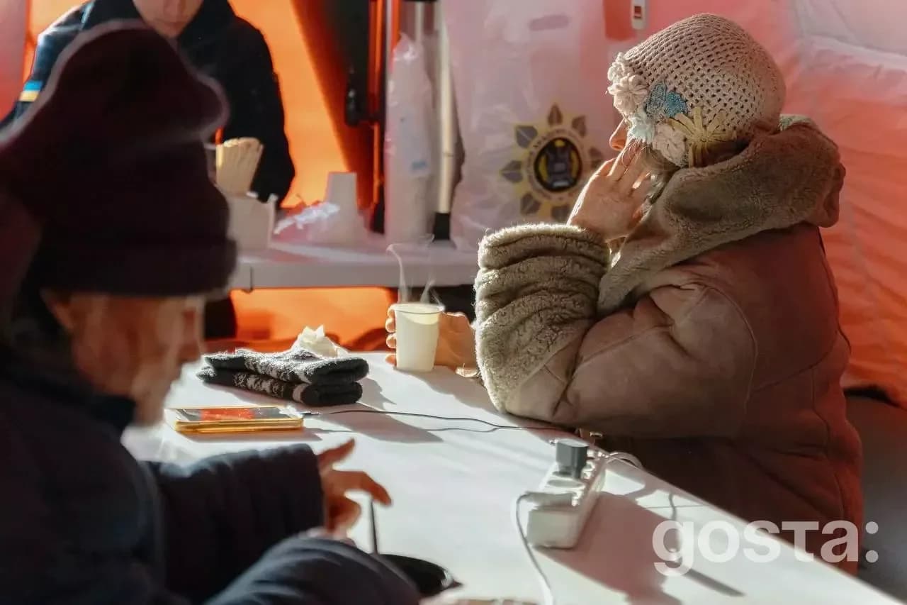 Люди в теплому одязі зігріваються в наметі обігріву з гарячими напоями під час кризи у місті.