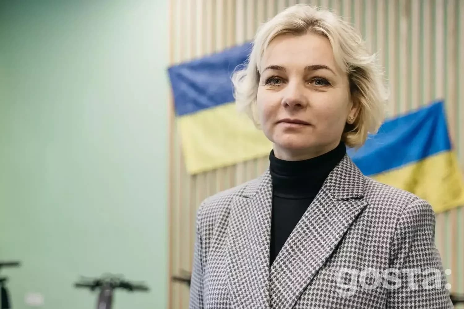 На зображенні жінка в діловому костюмі на фоні прапорів України в медичному центрі.