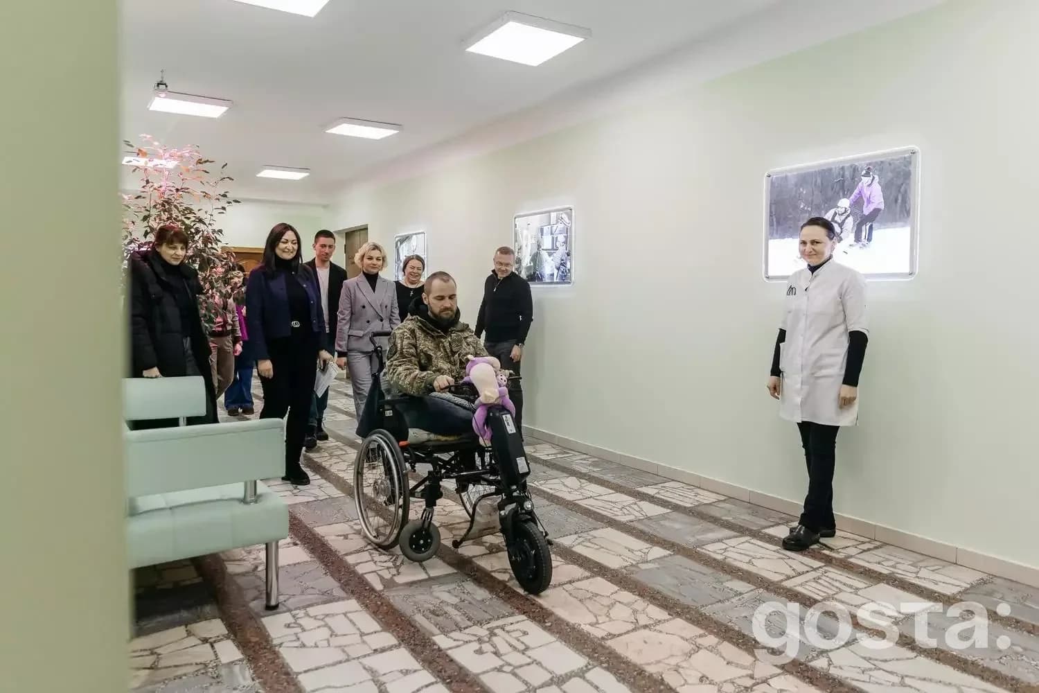 Користувач на інвалідному візку з електроприводом у клініці, супроводжуваний людьми, демонструє нову технологію реабіліт