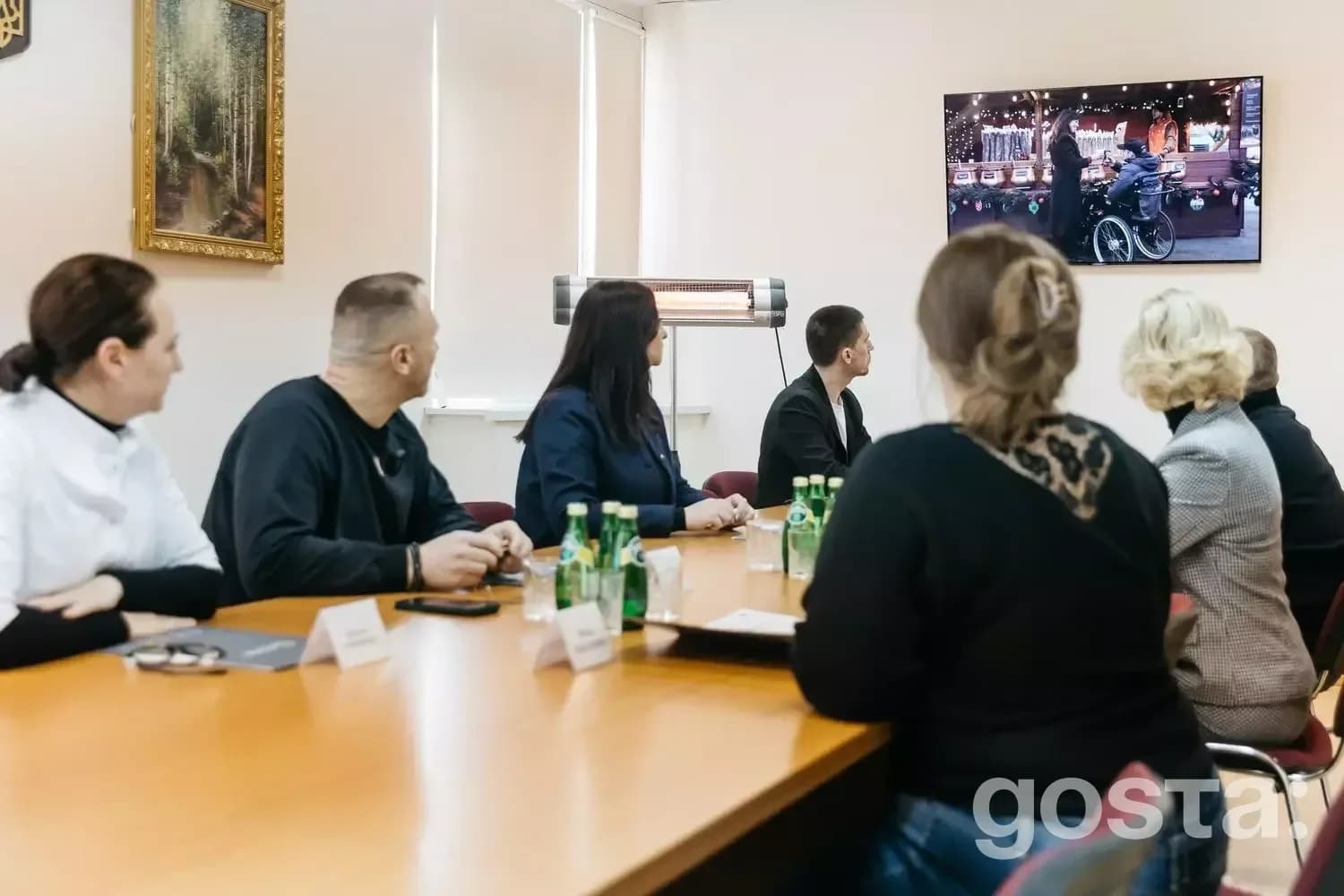 Група людей дивиться презентацію на екрані про використання електроприводів для крісел колісних у реабілітації.