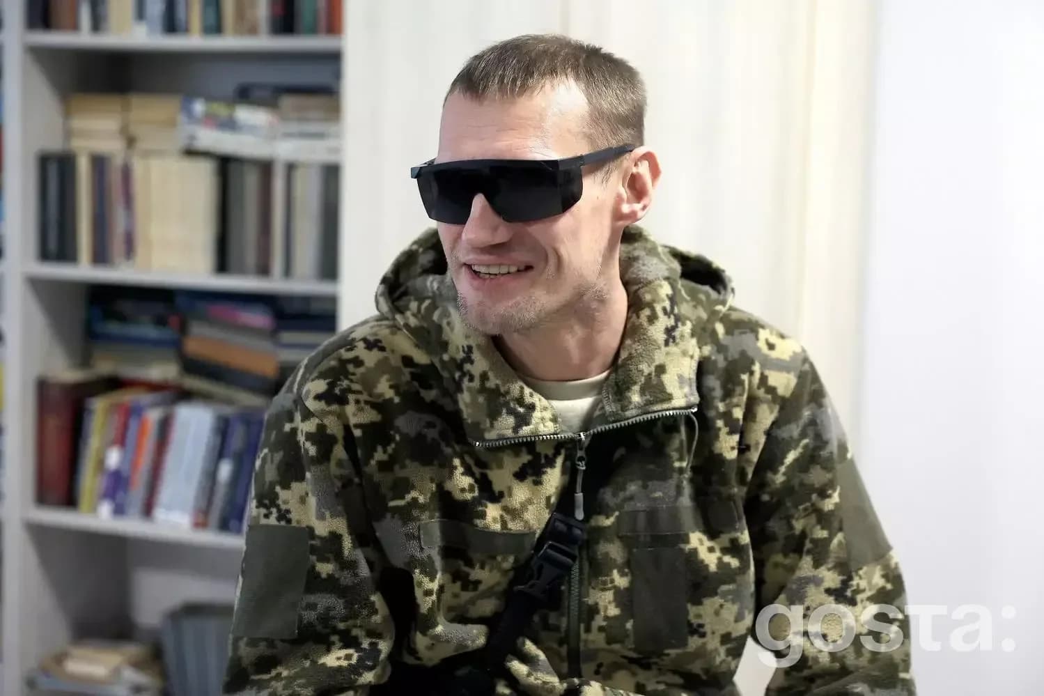 На зображенні ветеран у камуфляжі та темних окулярах, сидить у медичному реабілітаційному центрі.