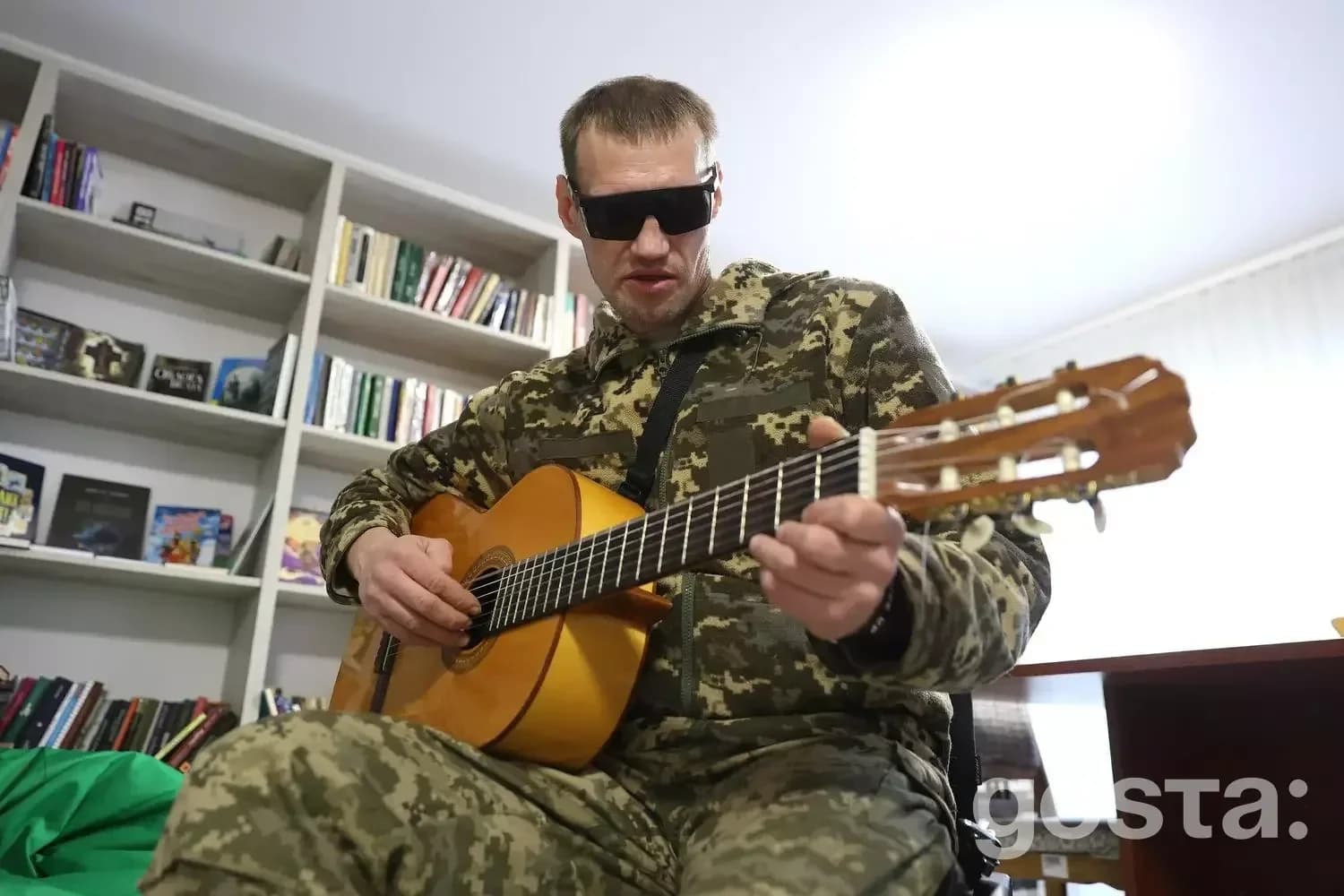 Ветеран у камуфляжній формі грає на гітарі в реабілітаційному центрі, зосереджений на арт-терапії для ветеранів.