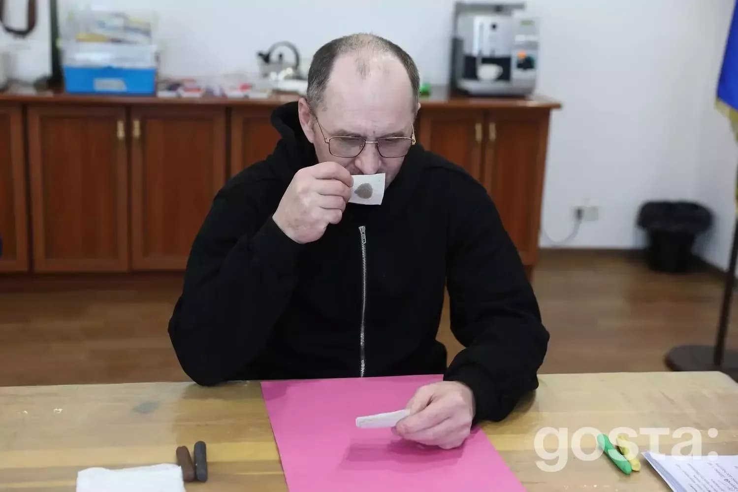Чоловік у медичному центрі п'є каву за столом, тримаючи картку з текстом, у контексті реабілітації ветеранів.
