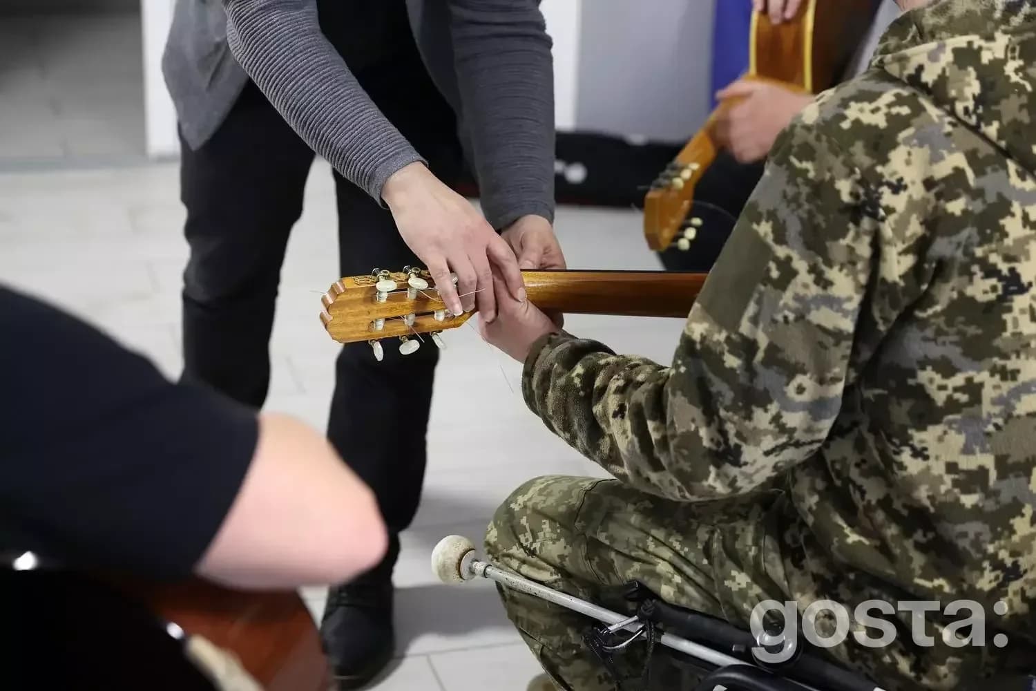 Учасник у військовій формі вчиться грати на гітарі під час реабілітації ветеранів у центрі «Пуща-Водиця».