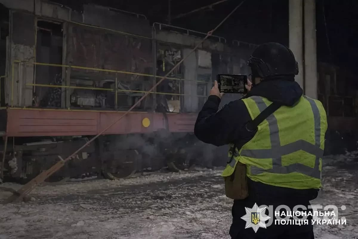 Співробітник поліції фіксує наслідки обстрілів в Україні; постраждалий об'єкт у нічній атмосфері.