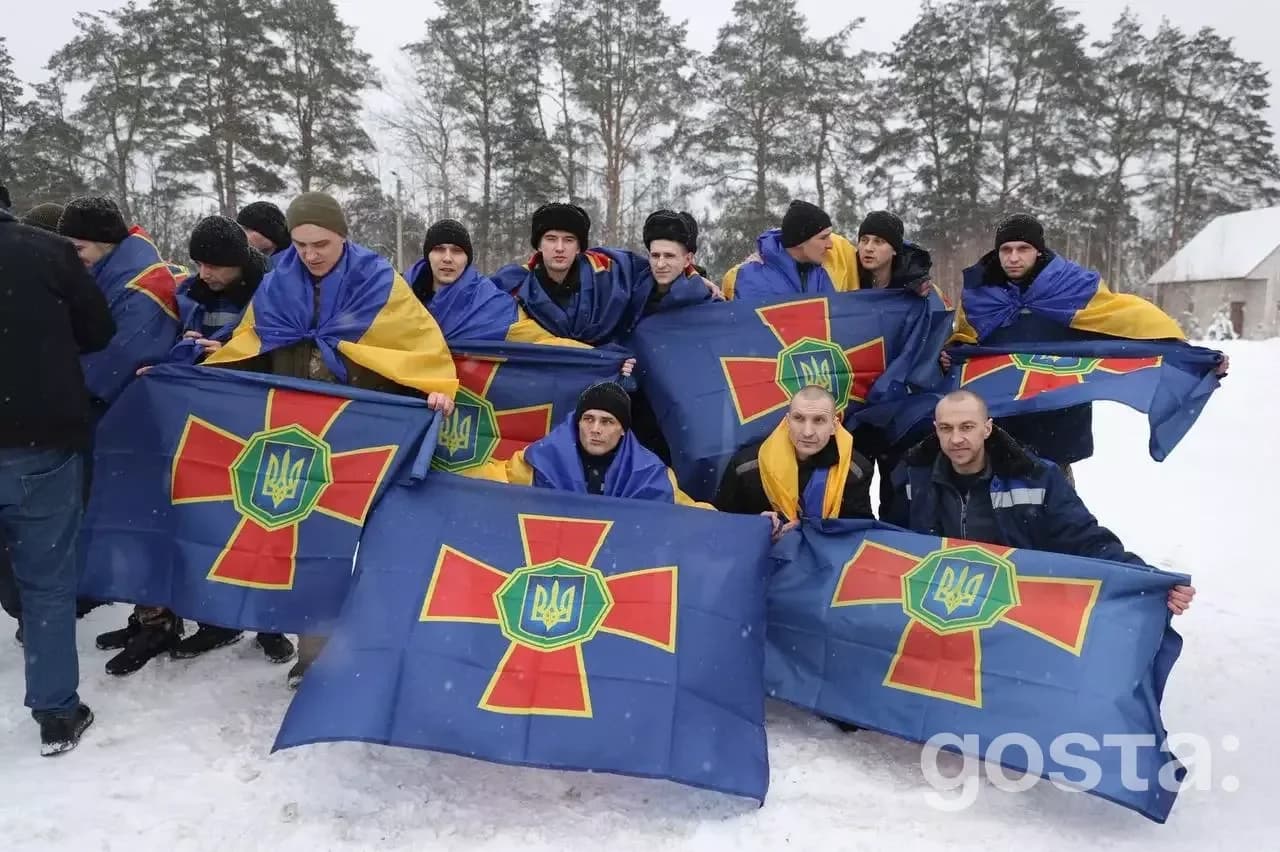 Група військовослужбовців із прапорами України, радіють поверненню додому після обміну полоненими.
