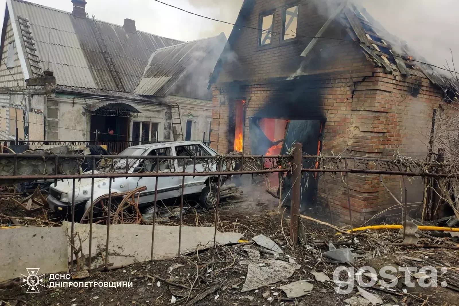 Будинок в Україні після обстрілу: пошкодження автомобіля та фасаду, полум'я всередині будівлі, руйнування довкола.