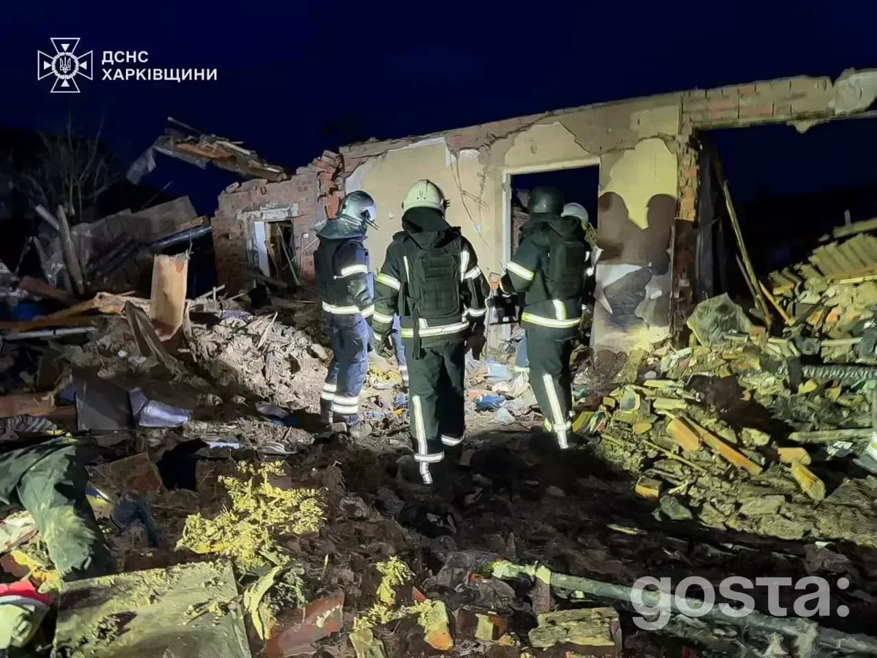 Троє рятувальників оглядають зруйновану внаслідок обстрілів будівлю вночі в Україні.
