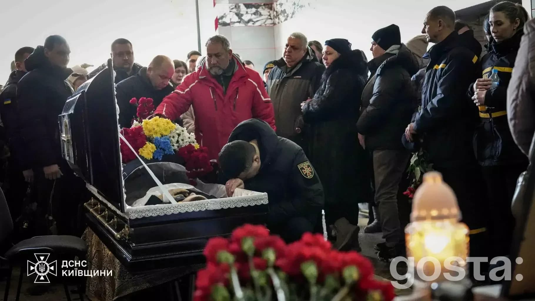 На фото група людей вшановує пам'ять рятувальника ДСНС України у траурній церемонії.
