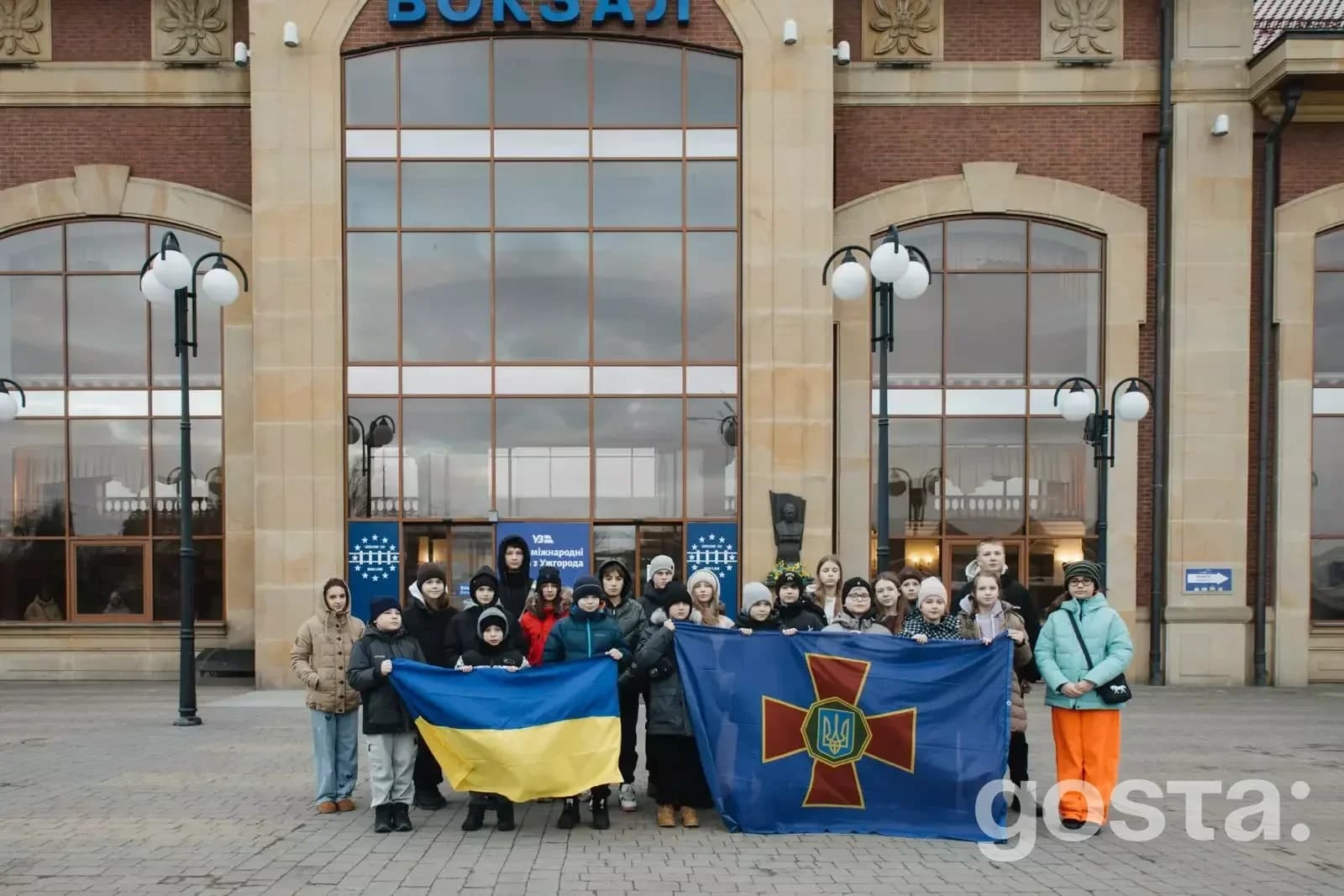 Група дітей військовослужбовців України з прапорами перед будівлею у Хорватії під час міжнародної програми підтримки.