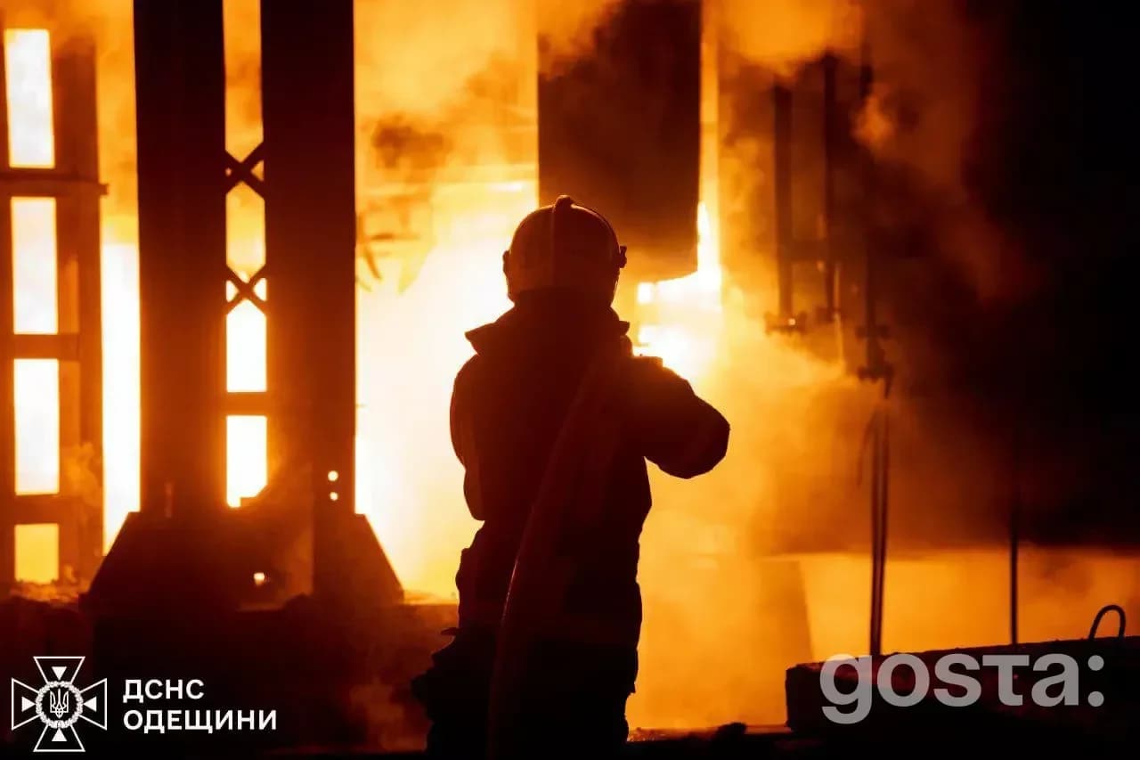 Рятувальник гасить пожежу на тлі вогню після російських ударів по Україні; роботи тривають вночі.