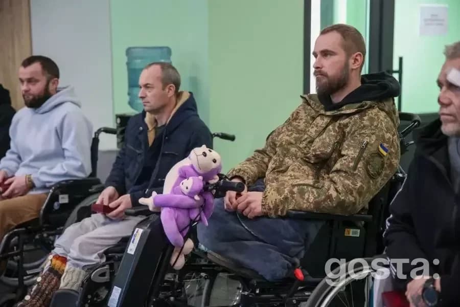 Четверо поранених українських нацгвардійців сидять на візках, один з них у військовій формі з патріотичним символом.