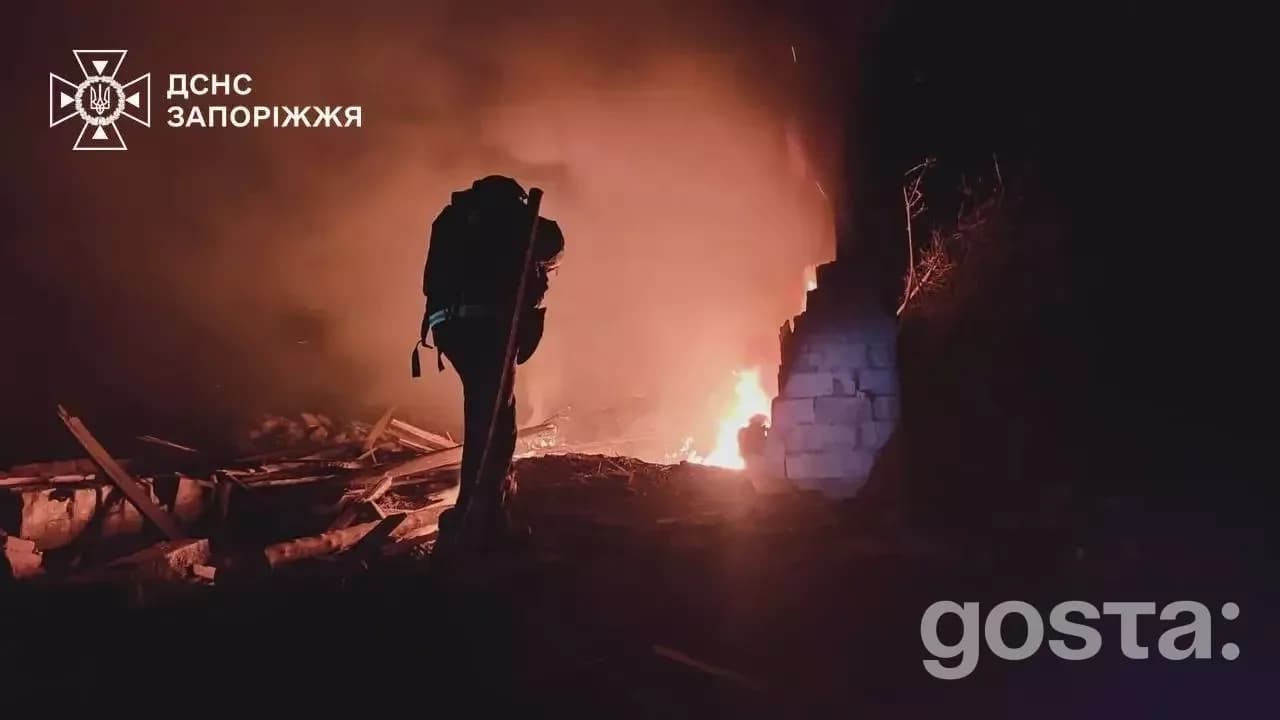 Рятувальник працює на фоні пожежі в Запоріжжі після атаки рф, видно зруйнований будинок і вогонь.