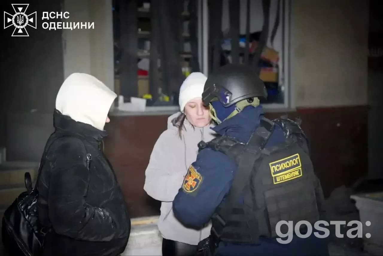 Рятувальник допомагає двом людям у шоломі на тлі зруйнованої будівлі після обстрілу в Україні.