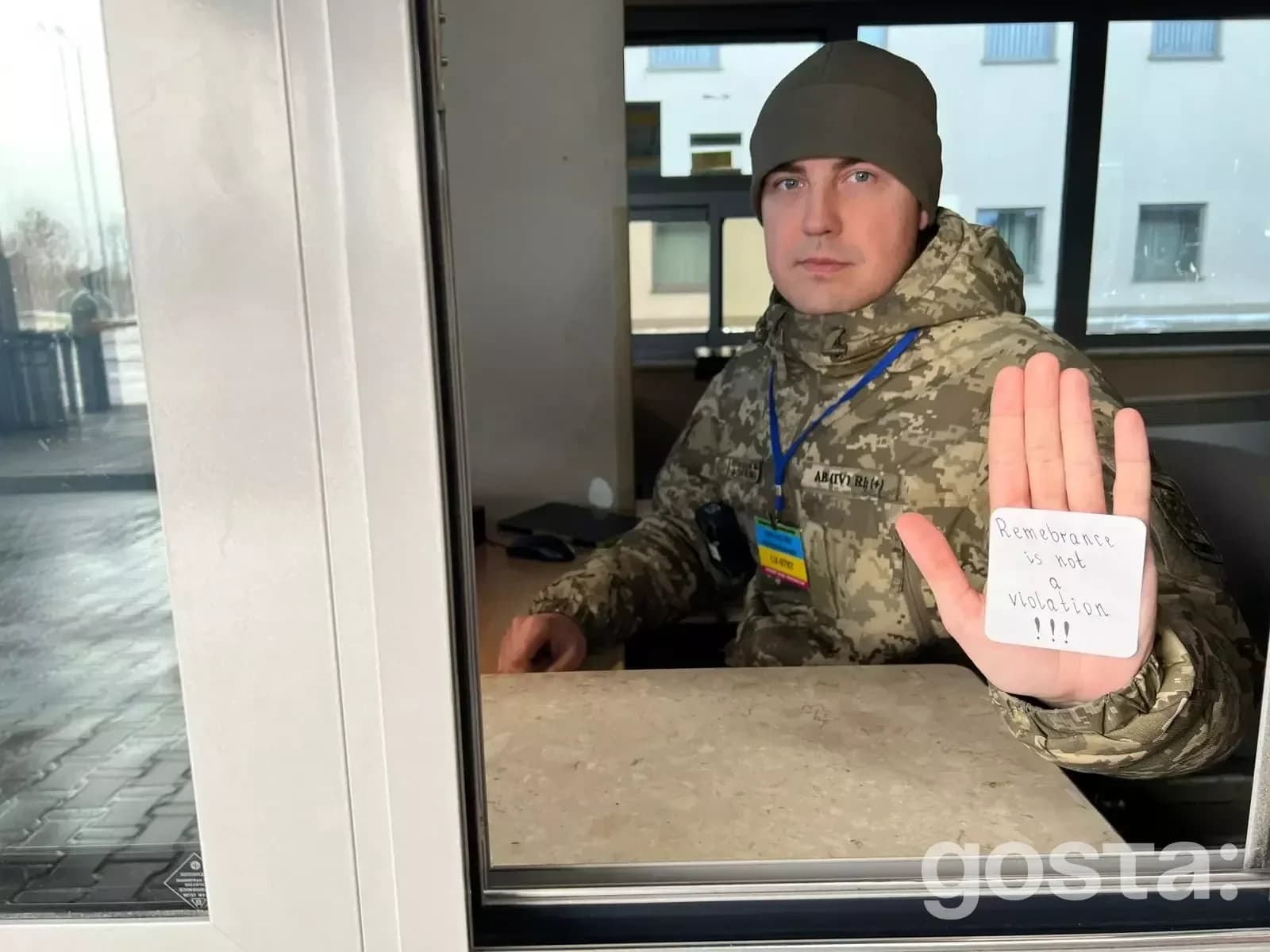 Військовослужбовець у формі тримає папірець з написом "Remembrance is not a violation" у приміщенні.