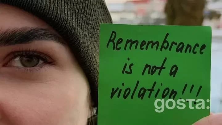 Людина тримає зелений папір із написом "Remembrance is not a violation" на фоні природи.