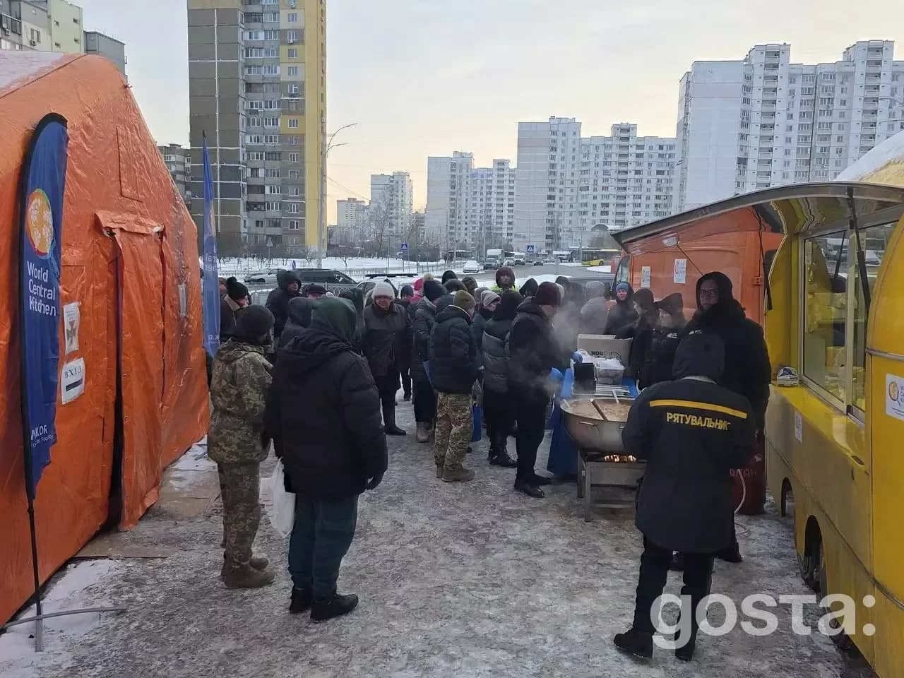 Люди збираються біля наметів обігріву в зимовому Києві з прапорами World Central Kitchen, ДСНС та Червоним Хрестом.