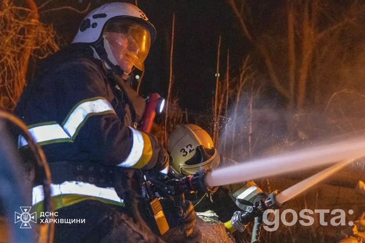 Firefighters battling a blaze at night, responding to attacks in Kharkiv region, highlighting war consequences.